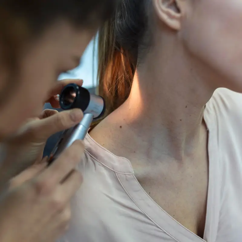 Dermatologist in latex gloves holding dermatoscope while examining attractive patient with skin disease Female dermatologist examining patient with dermascope looking for signs of skin cancer
